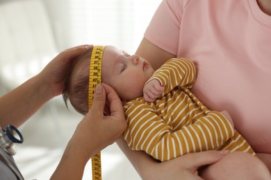 Photo of Mother and her cute little child having appointment with pediatrician in hospital. Doctor measuring baby's head, closeup