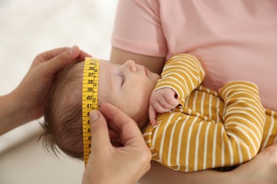 Photo of Mother and her cute little child having appointment with pediatrician in hospital. Doctor measuring baby's head, closeup