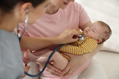 Photo of Mother and her cute little child having appointment with pediatrician in hospital. Doctor examining baby with stethoscope, closeup