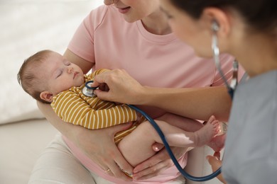 Photo of Mother and her cute little child having appointment with pediatrician in hospital. Doctor examining baby with stethoscope, closeup