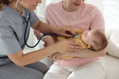 Photo of Mother and her cute little child having appointment with pediatrician in hospital. Doctor examining baby with stethoscope, closeup