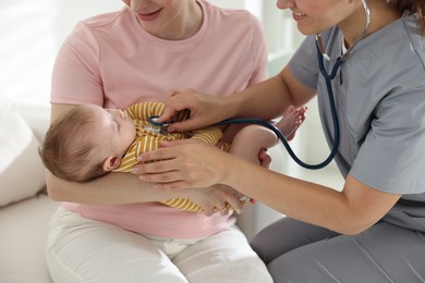 Photo of Mother and her cute little child having appointment with pediatrician in hospital. Doctor examining baby with stethoscope, closeup