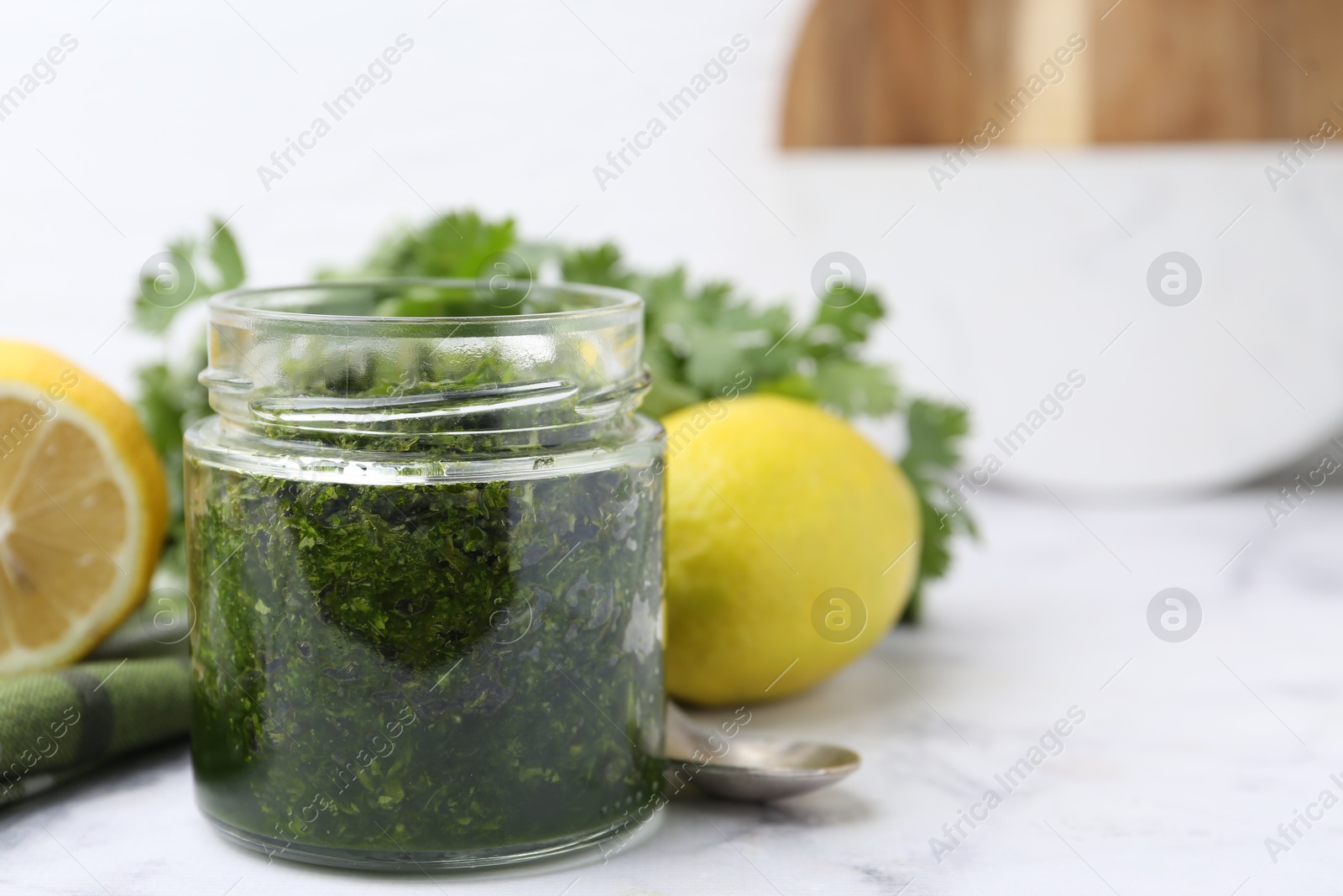 Photo of Tasty sauce with cilantro and lemons on white marble table, closeup. Space for text