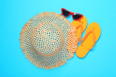 Photo of Straw hat, flip flops and sunglasses on light blue background, flat lay