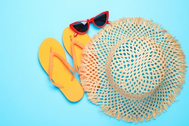 Photo of Straw hat, flip flops and sunglasses on light blue background, flat lay
