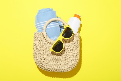 Photo of Wicker bag with beach towel and other summer accessories on yellow background, top view