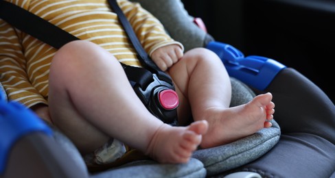 Photo of Cute little baby fastened in car seat, closeup