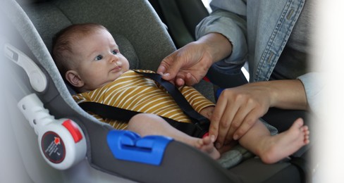 Photo of Mother fastening her baby in car seat, closeup