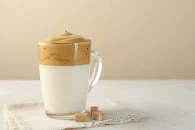 Photo of Delicious dalgona coffee in glass cup and brown sugar on light table, space for text