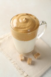Photo of Delicious dalgona coffee in glass cup and brown sugar on light table, closeup