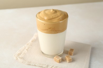 Photo of Delicious dalgona coffee in glass cup and brown sugar on light table, closeup