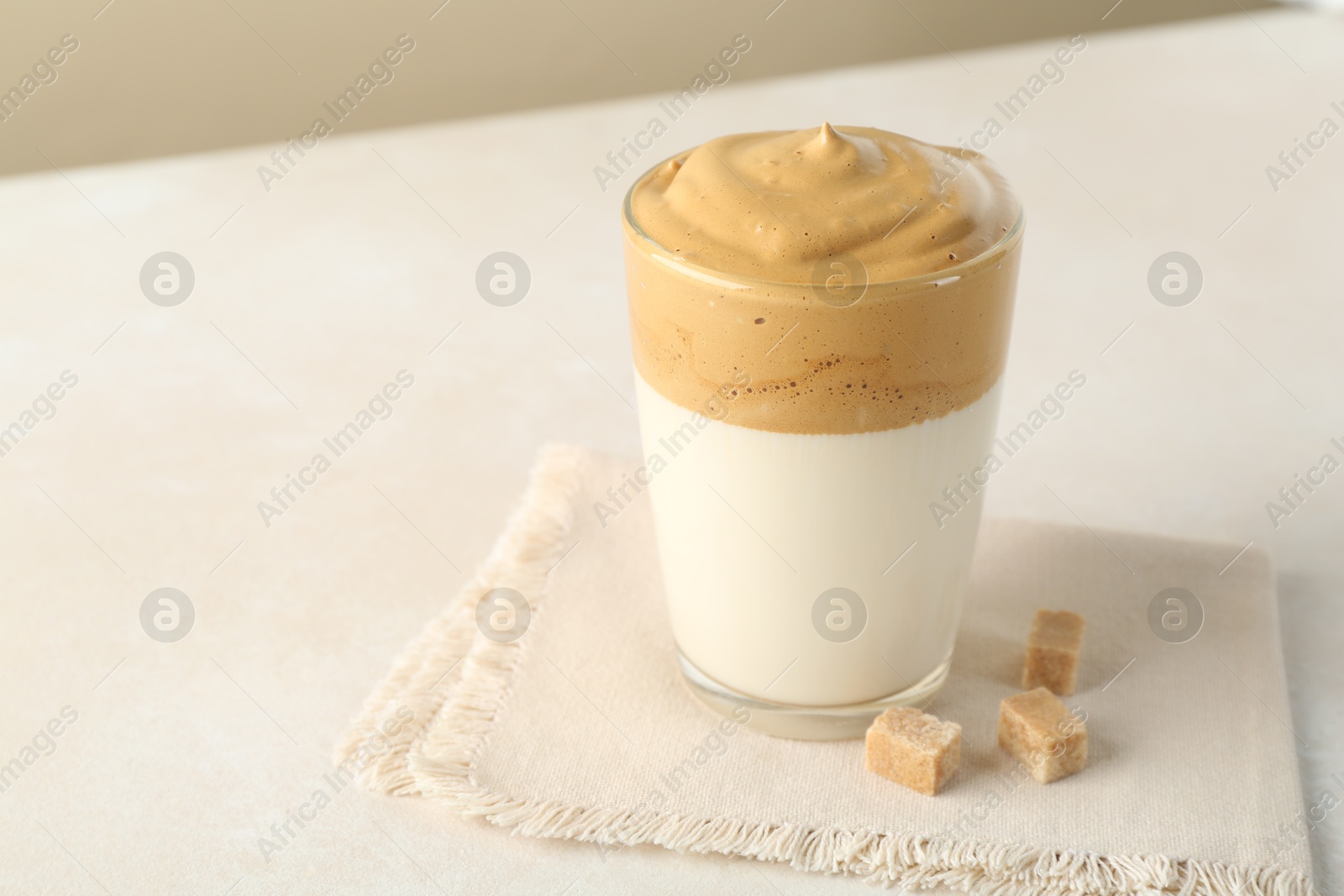 Photo of Delicious dalgona coffee in glass cup and brown sugar on light table, closeup. Space for text