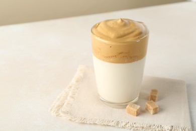Photo of Delicious dalgona coffee in glass cup and brown sugar on light table, closeup. Space for text