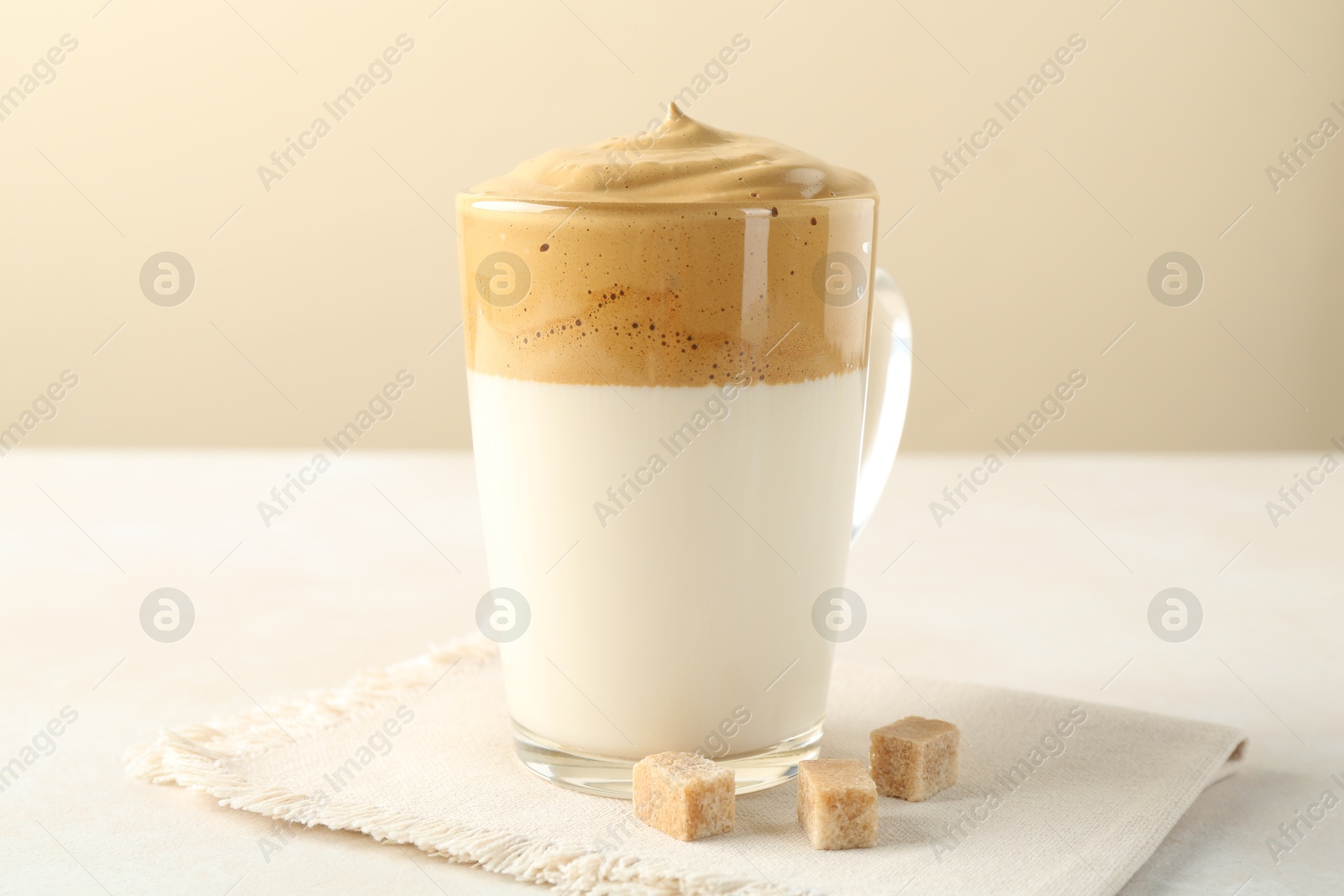 Photo of Delicious dalgona coffee in glass cup and brown sugar on light table, closeup