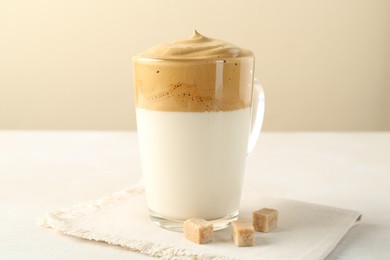 Photo of Delicious dalgona coffee in glass cup and brown sugar on light table, closeup