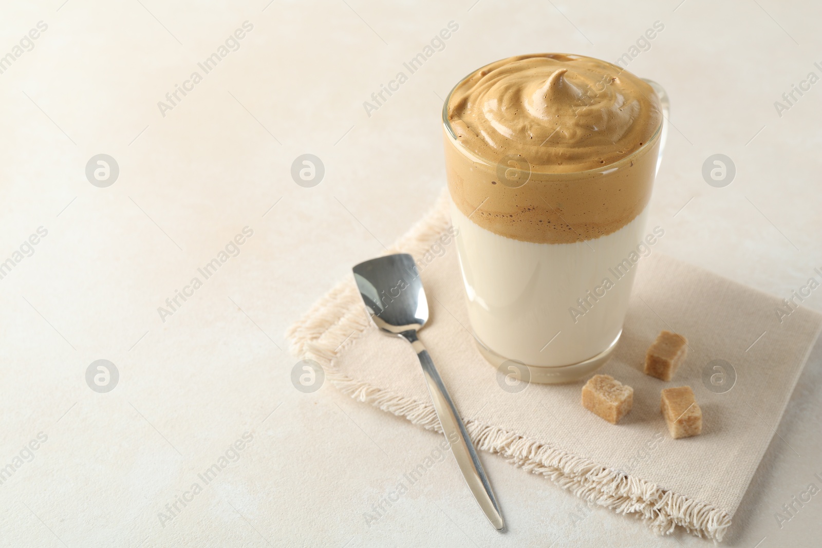 Photo of Delicious dalgona coffee in glass cup and brown sugar on light table, closeup. Space for text