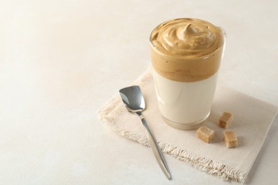 Photo of Delicious dalgona coffee in glass cup and brown sugar on light table, closeup. Space for text