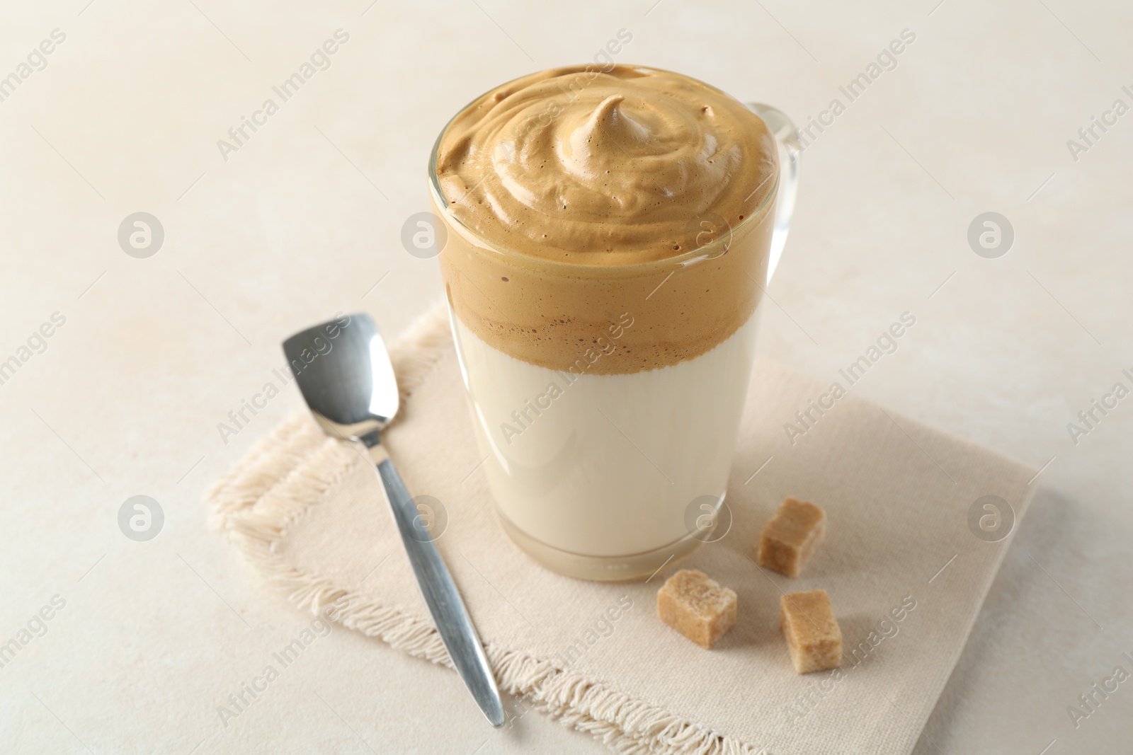 Photo of Delicious dalgona coffee in glass cup and brown sugar on light table, closeup