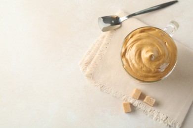 Photo of Delicious dalgona coffee in glass cup and brown sugar on light table, flat lay. Space for text