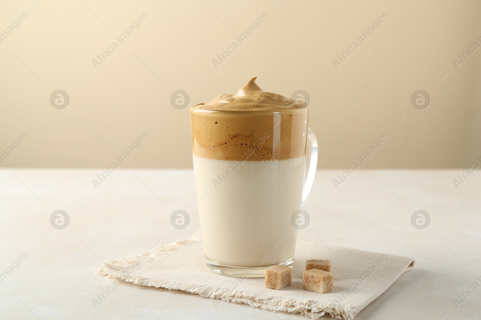 Photo of Delicious dalgona coffee in glass cup and brown sugar on light table