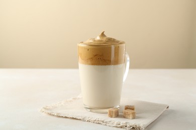Photo of Delicious dalgona coffee in glass cup and brown sugar on light table