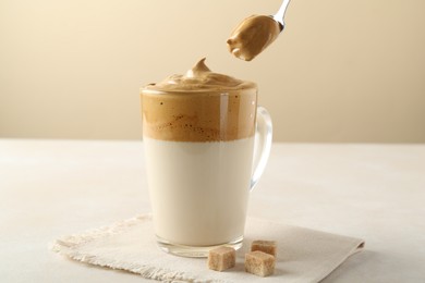 Photo of Taking cream from delicious dalgona coffee and brown sugar at light table, closeup
