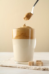 Photo of Taking cream from delicious dalgona coffee and brown sugar at light table, closeup