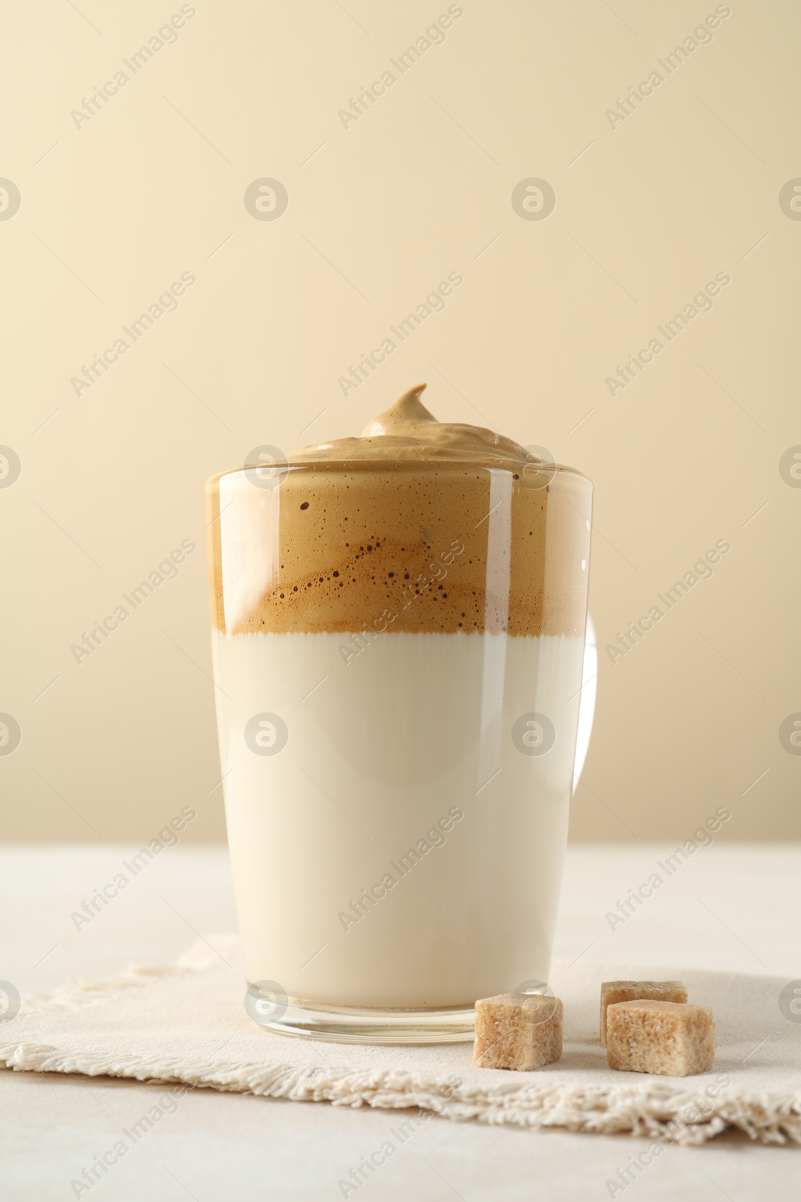 Photo of Delicious dalgona coffee in glass cup and brown sugar on light table, closeup