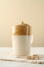 Photo of Delicious dalgona coffee in glass cup and brown sugar on light table, closeup
