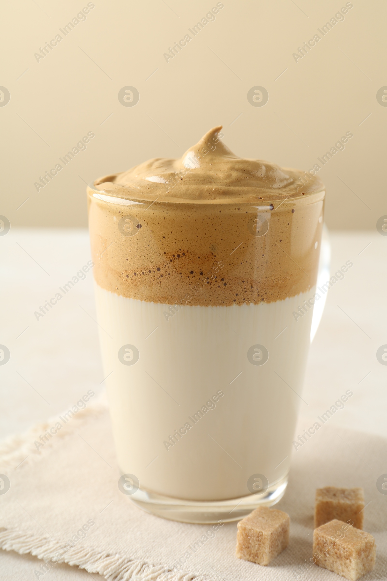Photo of Delicious dalgona coffee in glass cup and brown sugar on table, closeup