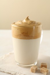 Photo of Delicious dalgona coffee in glass cup and brown sugar on table, closeup