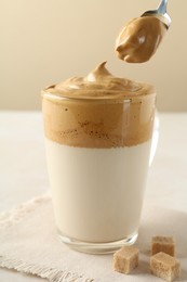 Photo of Taking cream from delicious dalgona coffee and brown sugar at light table, closeup