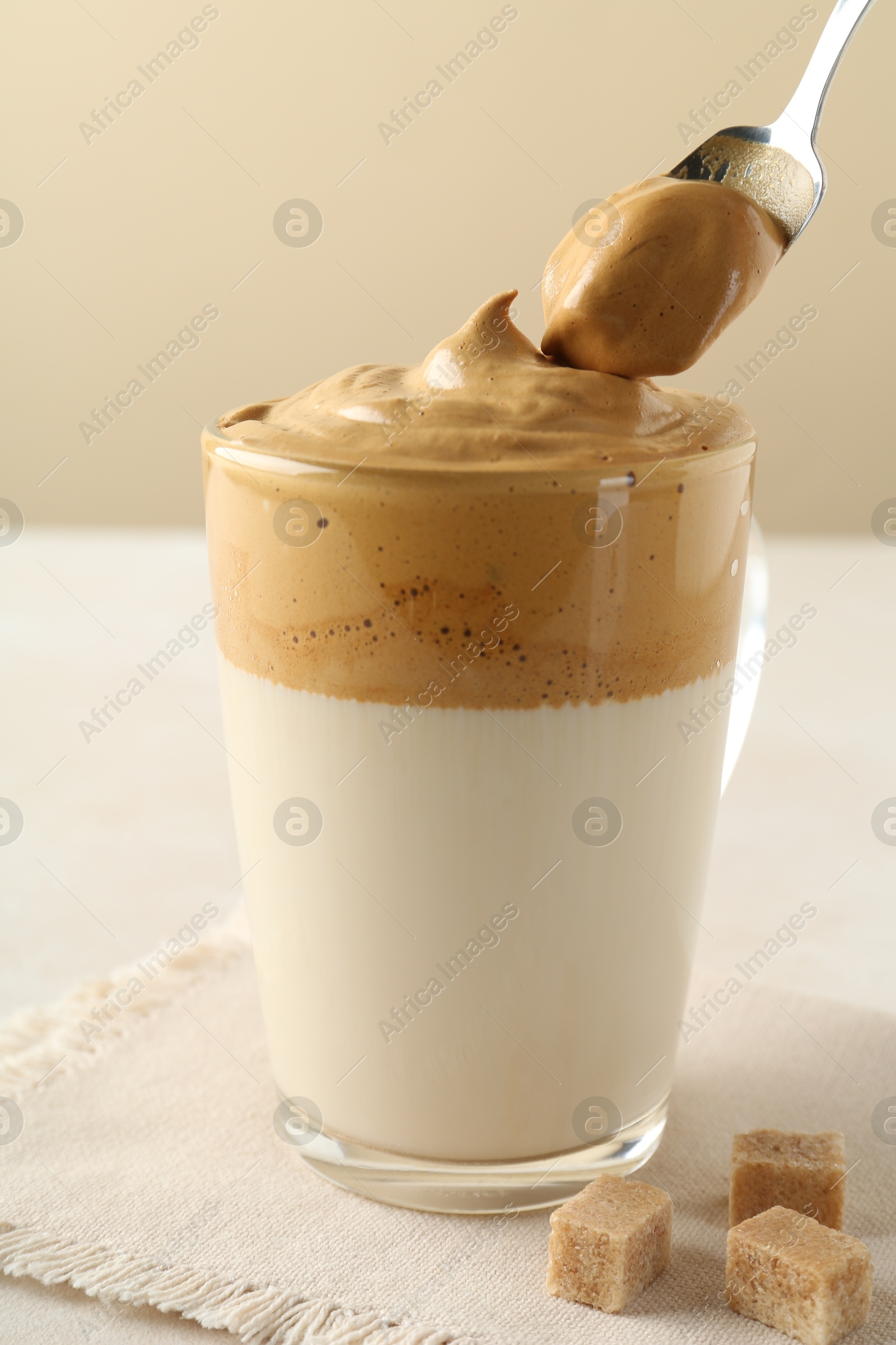 Photo of Taking cream from delicious dalgona coffee and brown sugar at light table, closeup