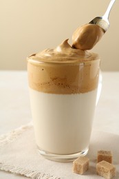 Photo of Taking cream from delicious dalgona coffee and brown sugar at light table, closeup