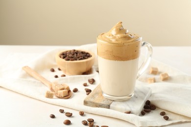 Photo of Delicious dalgona coffee in glass cup, beans and brown sugar on light table