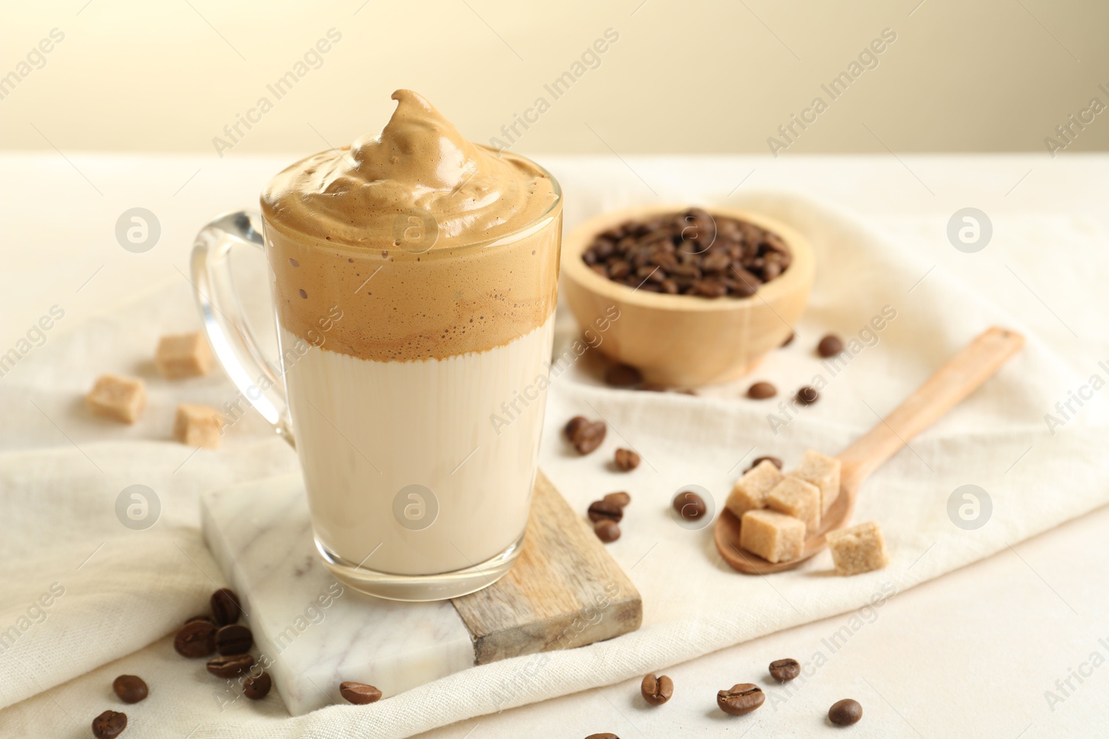 Photo of Delicious dalgona coffee in glass cup, beans and brown sugar on light table, closeup