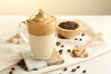 Photo of Delicious dalgona coffee in glass cup, beans and brown sugar on light table, closeup