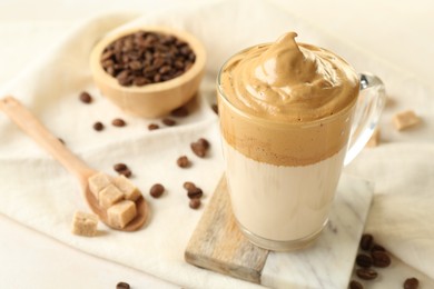 Photo of Delicious dalgona coffee in glass cup, beans and brown sugar on light table, closeup