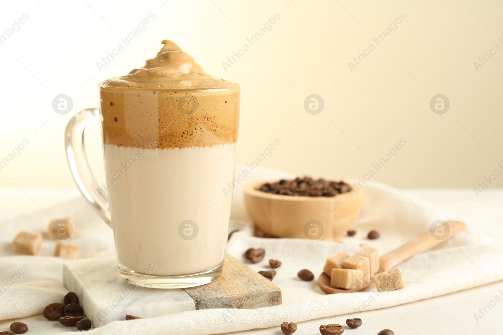 Photo of Delicious dalgona coffee in glass cup, beans and brown sugar on light table, closeup