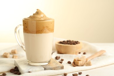 Photo of Delicious dalgona coffee in glass cup, beans and brown sugar on light table, closeup