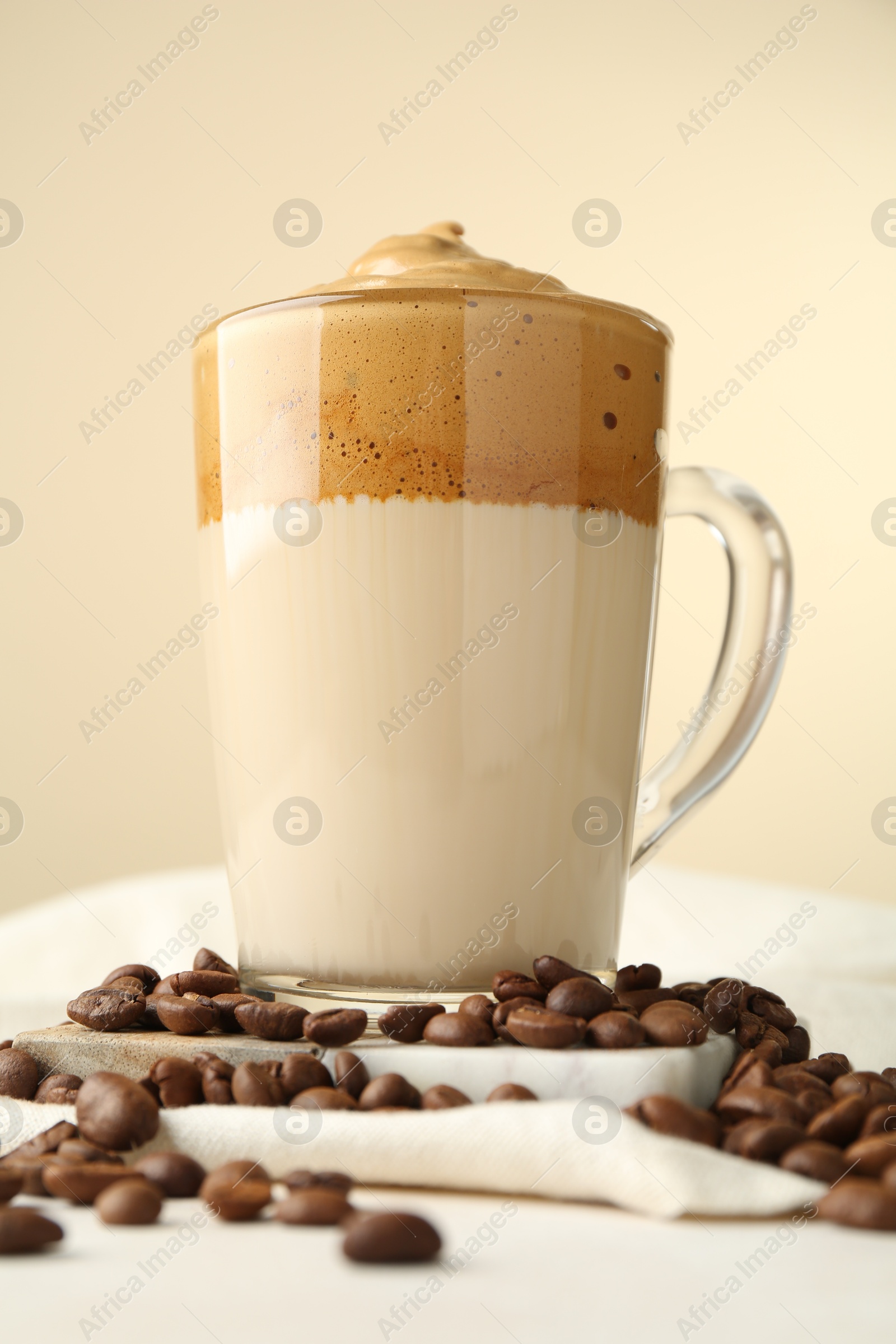 Photo of Delicious dalgona coffee in glass cup and beans on light table, low angle view