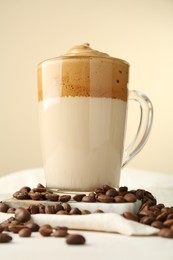 Photo of Delicious dalgona coffee in glass cup and beans on light table, low angle view