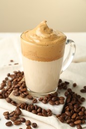 Photo of Delicious dalgona coffee in glass cup and beans on table, closeup