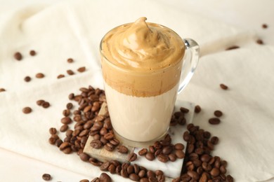 Photo of Delicious dalgona coffee in glass cup and beans on table, closeup