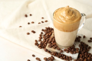 Photo of Delicious dalgona coffee in glass cup and beans on light table, closeup. Space for text