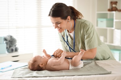 Photo of Mother and her cute little child having appointment with pediatrician in hospital. Doctor examining baby with stethoscope