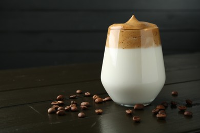 Photo of Delicious dalgona coffee in glass and beans on wooden table, closeup. Space for text
