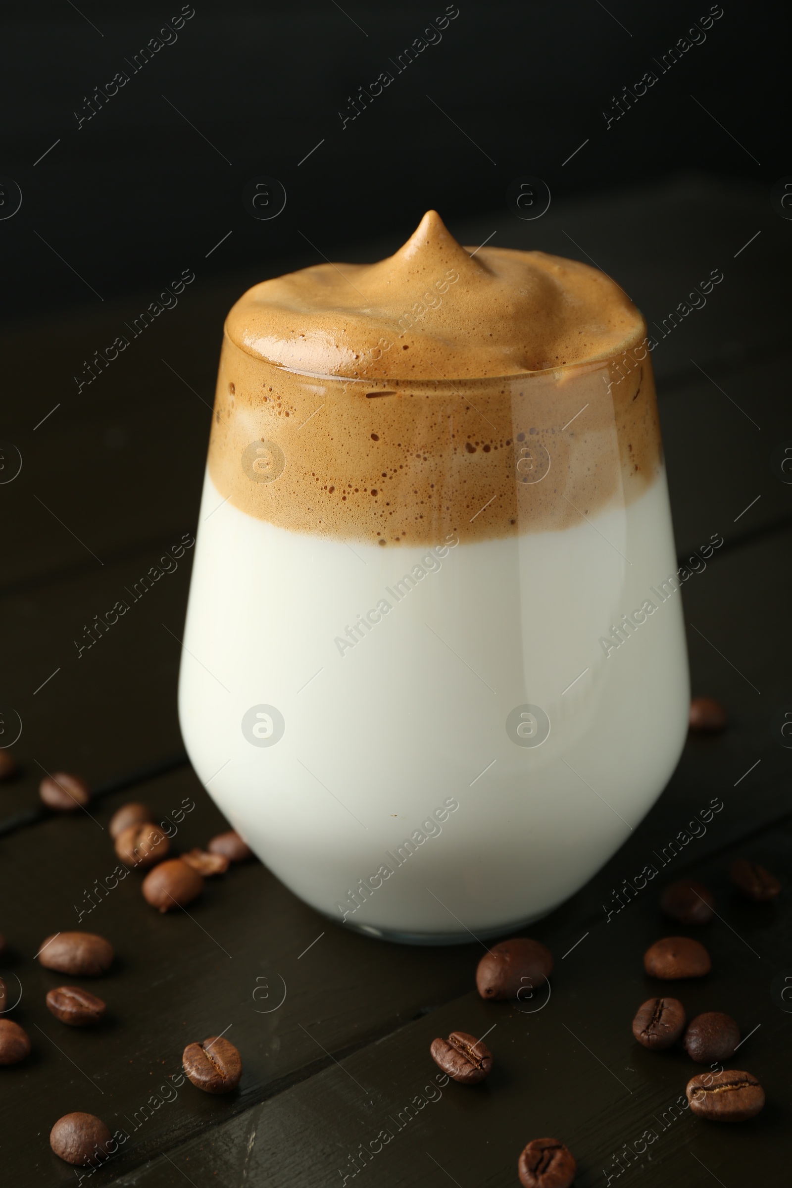 Photo of Delicious dalgona coffee in glass and beans on wooden table, closeup