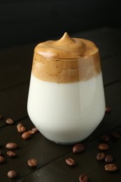 Photo of Delicious dalgona coffee in glass and beans on wooden table, closeup