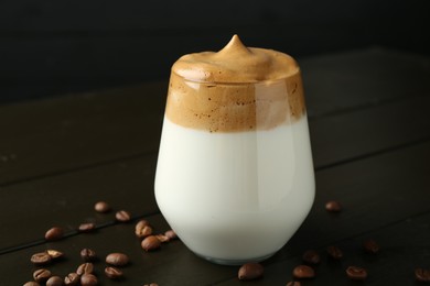Photo of Delicious dalgona coffee in glass and beans on wooden table, closeup